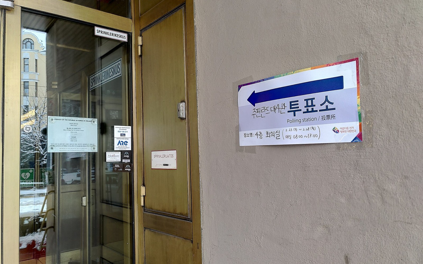 A polling station sign with an arrow points toward a building entrance in winter
